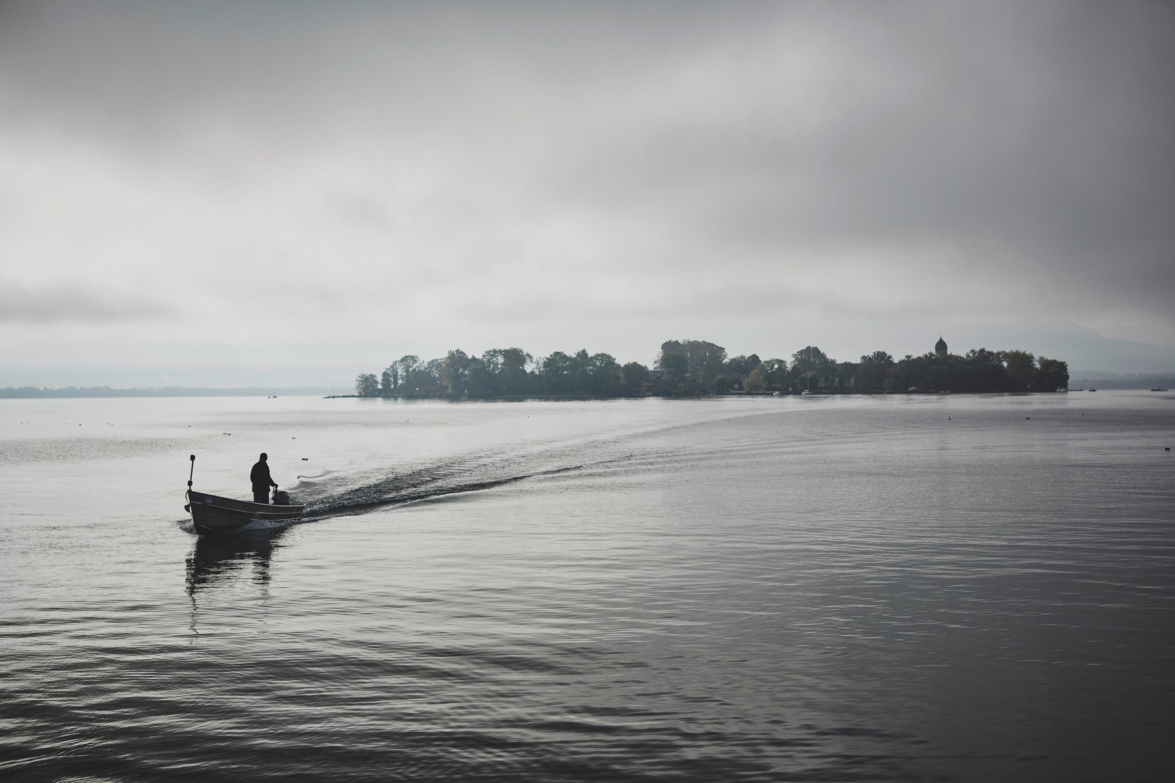 Fisherman steering a boat towards Frauenchiemsee on a grey morning