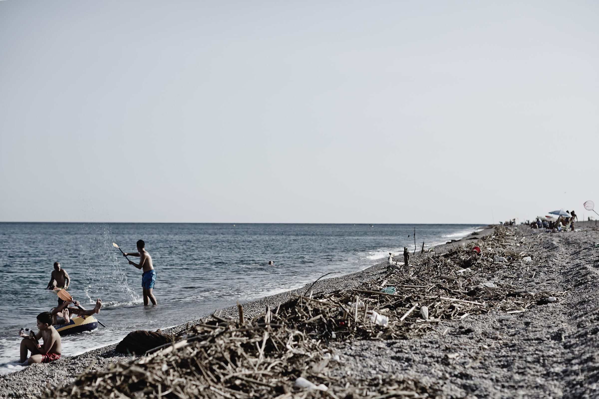 Children playing in the sea beside driftwood on a pebble beach near Almería